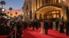 Film festival attendees and photographers gather on a red carpet outside a classic Hollywood movie palace at dusk.