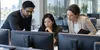 Three technology professionals review computer systems together in a modern office.