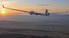 A long-winged uncrewed reconnaissance aircraft flying over an arid landscape at dawn