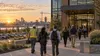 Workers enter a modern employment center at dawn with industrial and construction activity visible in the distance.