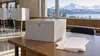 Generic ballot box and blank ranked-choice ballots in an Alaska civic hall with snowy mountains outside.