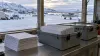 Plain ballot envelopes and secure mail trays in a rural Alaska air-cargo facility, with a bush plane and snowy village outside.