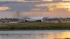 A generic twin-engine cargo aircraft disabled beyond an airport runway as fire-rescue vehicles respond at a distance.