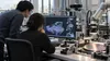 Two engineers study a spatial model beside robotics equipment and a silicon wafer in a research lab.