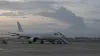 An unbranded passenger aircraft on a tropical airport apron with a distant volcanic ash plume