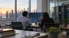 Two anonymous analysts reviewing unlabeled market charts in a modern office beside a glass-walled server room