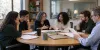 Graduate psychology trainees and faculty review materials around a seminar table in a university training room.