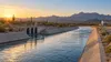 A concrete-lined water canal carries water through an arid Arizona desert landscape at sunrise.