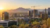 A Phoenix-area business district with office buildings and a construction crane against desert mountains at sunrise.