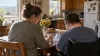 A caregiver and an adult wheelchair user work on a puzzle together at a kitchen table in a sunlit Arkansas home.