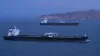 Two unmarked crude-oil tankers crossing calm blue water near the rocky Omani coast at blue hour