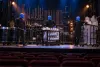 Three blue-painted percussion performers on a theater stage with custom tubular instruments