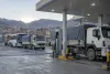 Cargo trucks and a bus wait at an unbranded fuel station in La Paz at dawn.