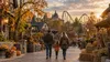 A family walks through an autumn-decorated European-style theme park near sunset, with a roller coaster in the distance.