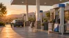 An unbranded California fuel station with several pumps and a passenger car in warm evening light.