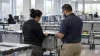 Election workers inspect sealed ballot containers in a county election processing room.
