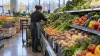 A grocery employee restocks fresh produce in a modern supermarket aisle.