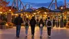 Illustrative evening view of an adult chaperone and a small group of teenagers approaching a generic amusement-park entrance.