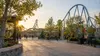 A quiet amusement-park plaza with modern steel roller-coaster track in warm morning light.