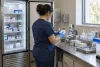 Healthcare worker reviewing vaccine inventory beside a clinic refrigerator