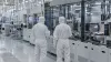 Two technicians inspect wafer-processing equipment in an anonymous semiconductor cleanroom.