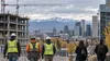 Workers stand near a Colorado construction and office district with the Rocky Mountains beyond.