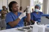A health worker prepares an unlabeled vaccine dose inside a temporary clinic while a colleague waits nearby.