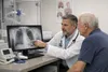 Photorealistic pulmonology clinic scene with a physician reviewing non-readable lung imaging beside an adult patient, in a neutral medical setting with no logos or identifiable records.