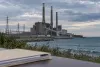 A large coal-fired power station and transmission lines beside Lake Michigan under an overcast sky, with an unmarked legal folder in the foreground.