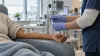 A clinician checks an IV infusion line beside a patient’s arm in a modern clinical research suite.