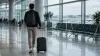 A business traveler walks through an airport concourse with a roller suitcase.