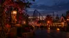 An autumn amusement park midway at dusk with pumpkins, warm lights and a roller coaster silhouette
