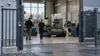 Technicians walk through a secured industrial workshop containing an unmanned ground robotics platform.