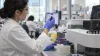 A clinical laboratory professional examines a blood sample beside an automated analyzer.