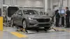 A sedan undergoes fuel-economy testing on a chassis dynamometer as technicians monitor equipment.