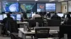 Emergency-management professionals monitor storm and wildfire maps in a partially staffed operations center.