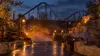 A foggy amusement-park walkway with roller coaster silhouettes under evening lights