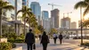Anonymous commuters walk through a Florida business district with office towers and construction cranes at sunrise.