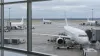 Several unbranded passenger jets sit at airport gates as another aircraft taxis under an overcast sky.