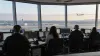 Air traffic controllers monitor communications consoles in a modern control facility as an aircraft approaches in daylight.
