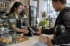 A customer uses an unbranded smartphone at a Southeast Asian retail counter while a merchant processes the transaction.