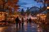 An autumn amusement park midway at dusk with pumpkins, warm lights and a wooden roller coaster in the background