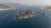 Aerial editorial view of a barren island dividing a narrow sea passage as an oil tanker and cargo ship transit on opposite sides.