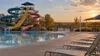 Empty outdoor water park with colorful slides and unoccupied lounge chairs under a late-summer sky