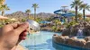 A hand holding a plain silver admission wristband at a generic desert water park