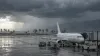 Unbranded passenger aircraft on a rain-swept tropical airport apron beneath dark storm clouds.