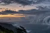 Dark rain bands over rough ocean near a wind-swept Hawaiʻi coastline before dawn