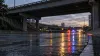 Illustrative view of an empty urban roadway beneath an overpass with distant emergency-light reflections at dusk