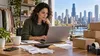 Illinois small-business owner reviewing online sales records with shipping boxes nearby.