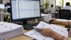 Election worker reviews voter registration records beside a computer database in an administrative office